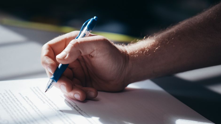 Detailed shot of a hand holding a blue pen while signing a document.