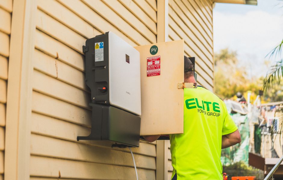 Electrician from Elite Power Group inspecting a solar inverter outside.