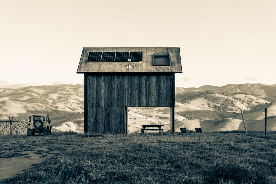 A rustic barn with solar panels, set against rolling hills and a vintage car.