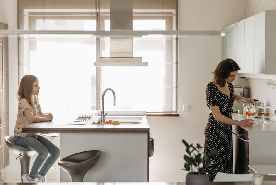 A mother pours juice in a modern kitchen while her daughter watches.