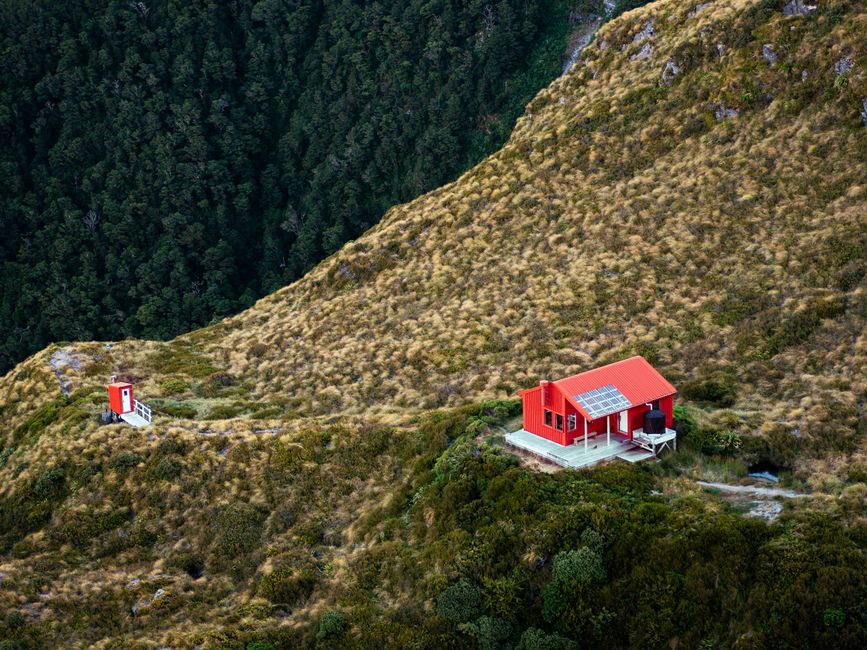 Aerial view of a vibrant red cabin in a lush, remote mountain landscape.