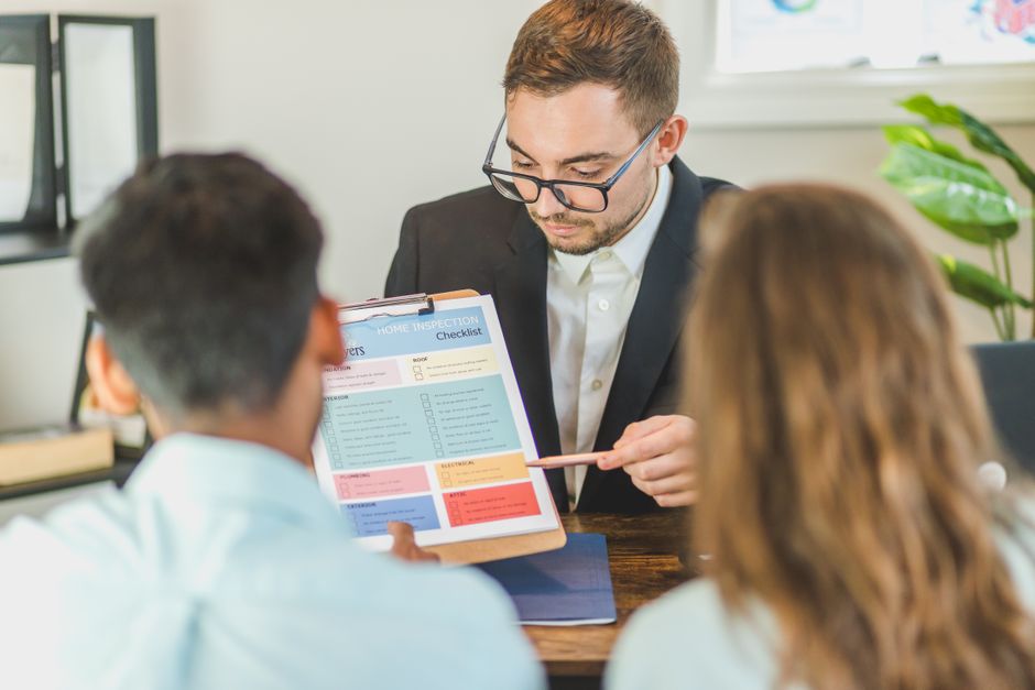 Real estate agent explaining a home inspection checklist to clients in an office setting.